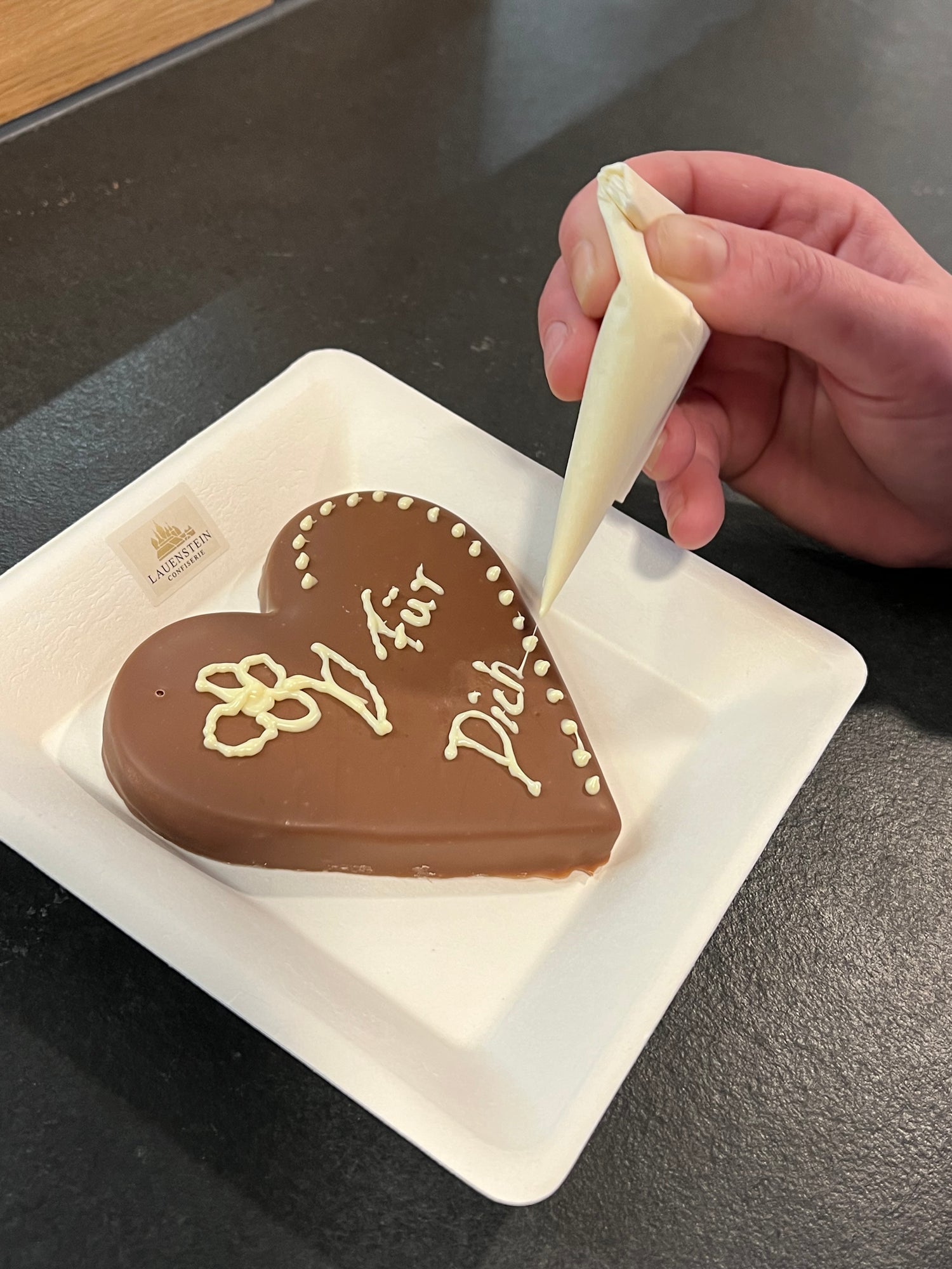 Hand verziert eine herzförmige Schokolade mit weißer Glasur – Einblick in die Manufaktur der Lauenstein Confiserie beim Besuch.