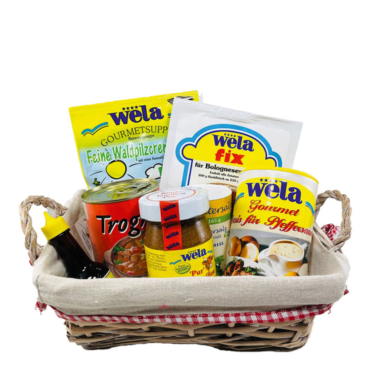 Wela Präsentkorb Classic mit verschiedenen Produkten – Gläser, Beutel und eine kleine Flasche im Weidenkorb.