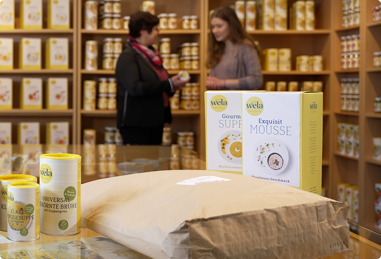 Innenansicht des Wela Werksverkaufs in Ludwigsstadt mit gelb etikettierten Suppen- und Würzprodukten, Verkaufsregalen und Beratungssituation 